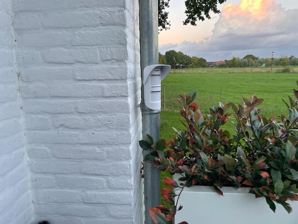 Buitendetector aan een witte gevel met zicht op het weiland