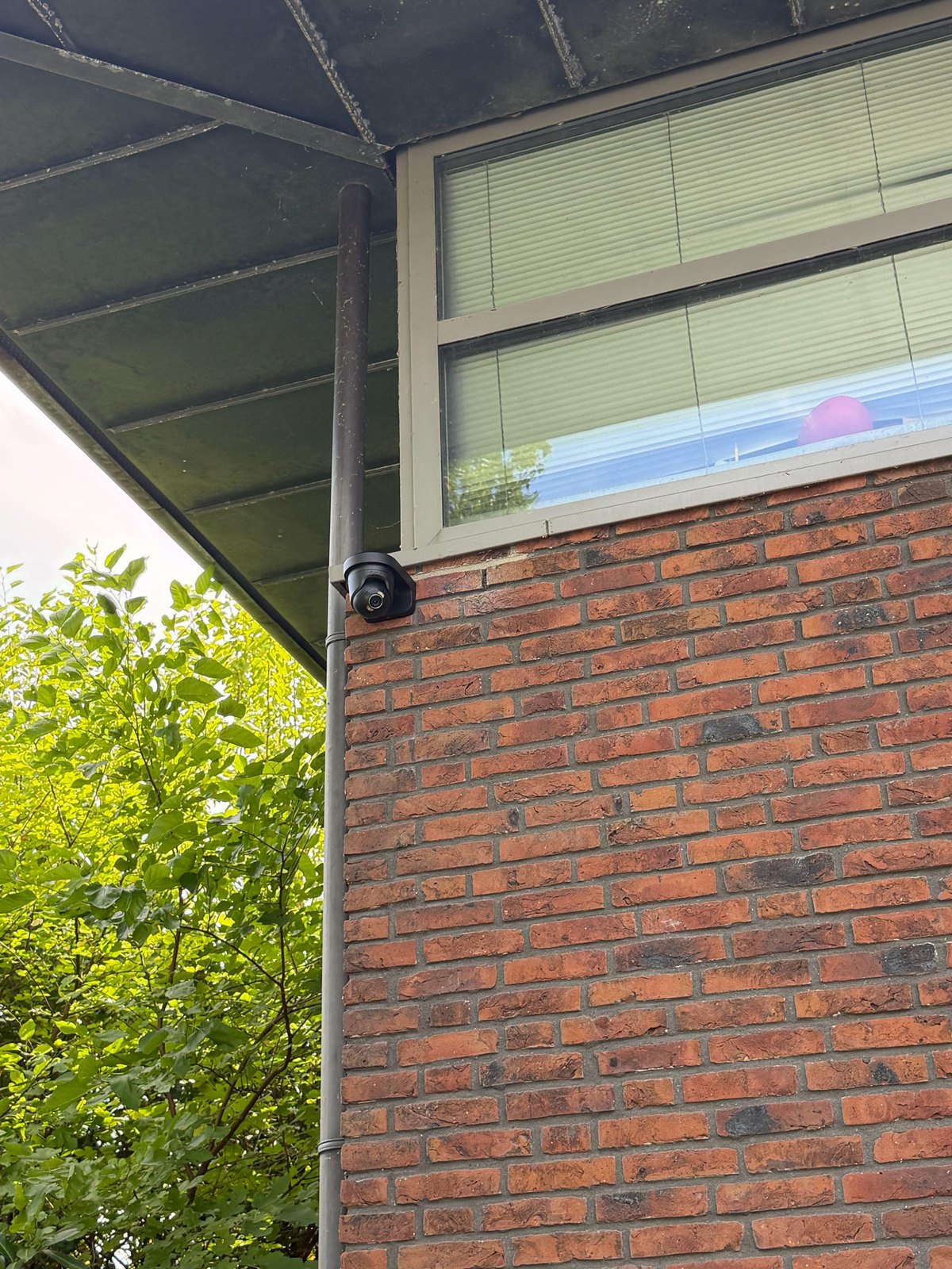 Zwarte camera onder de dakoverstek naast de regenpijp