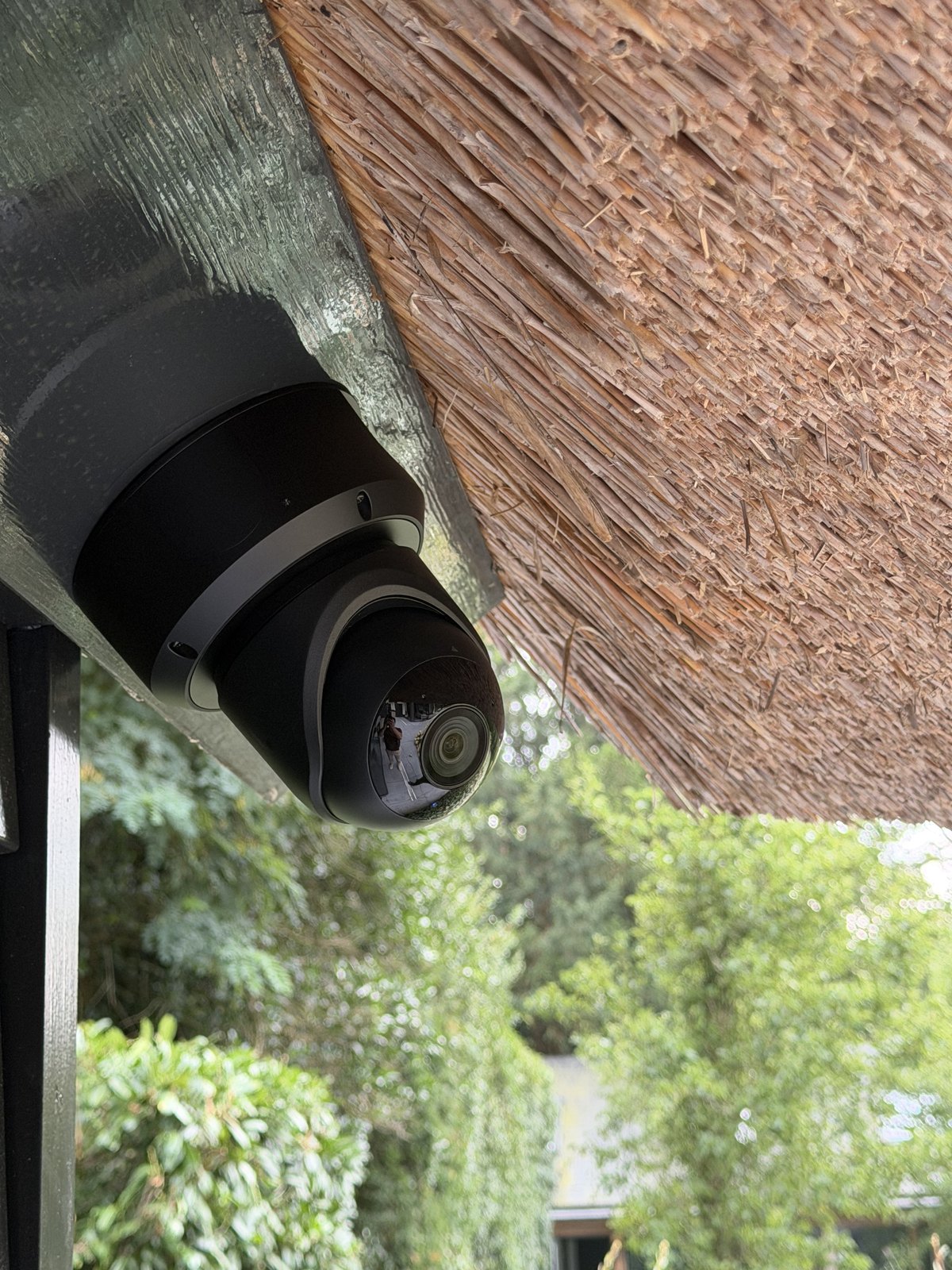 Zwarte camera weggewerkt onder de rand van een rieten dak