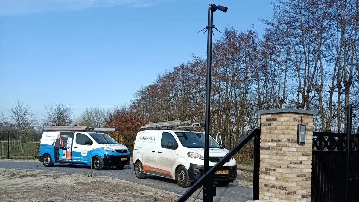 Zwarte camerapaal naast een gemetselde poortpijler met intercom bij een inrit