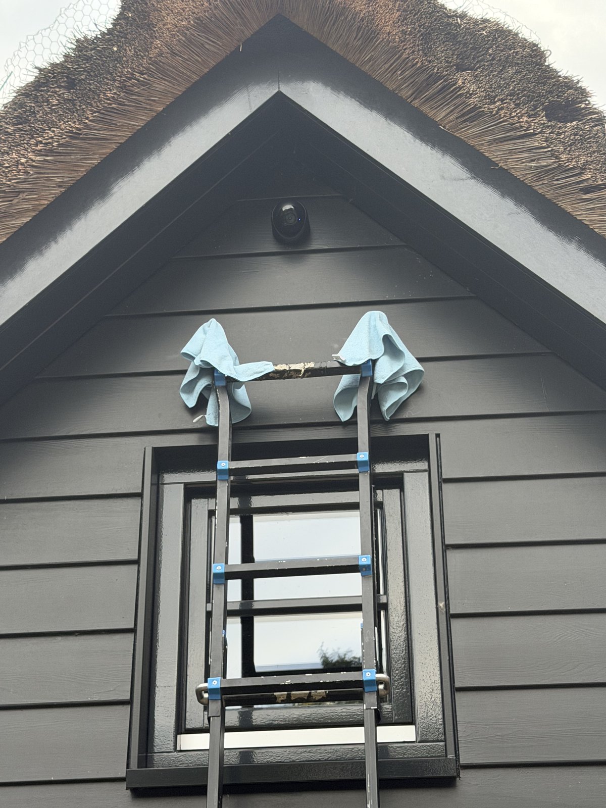 Ladder met doeken om de uiteinden tegen een zwarte houten gevel, camera al gemonteerd
