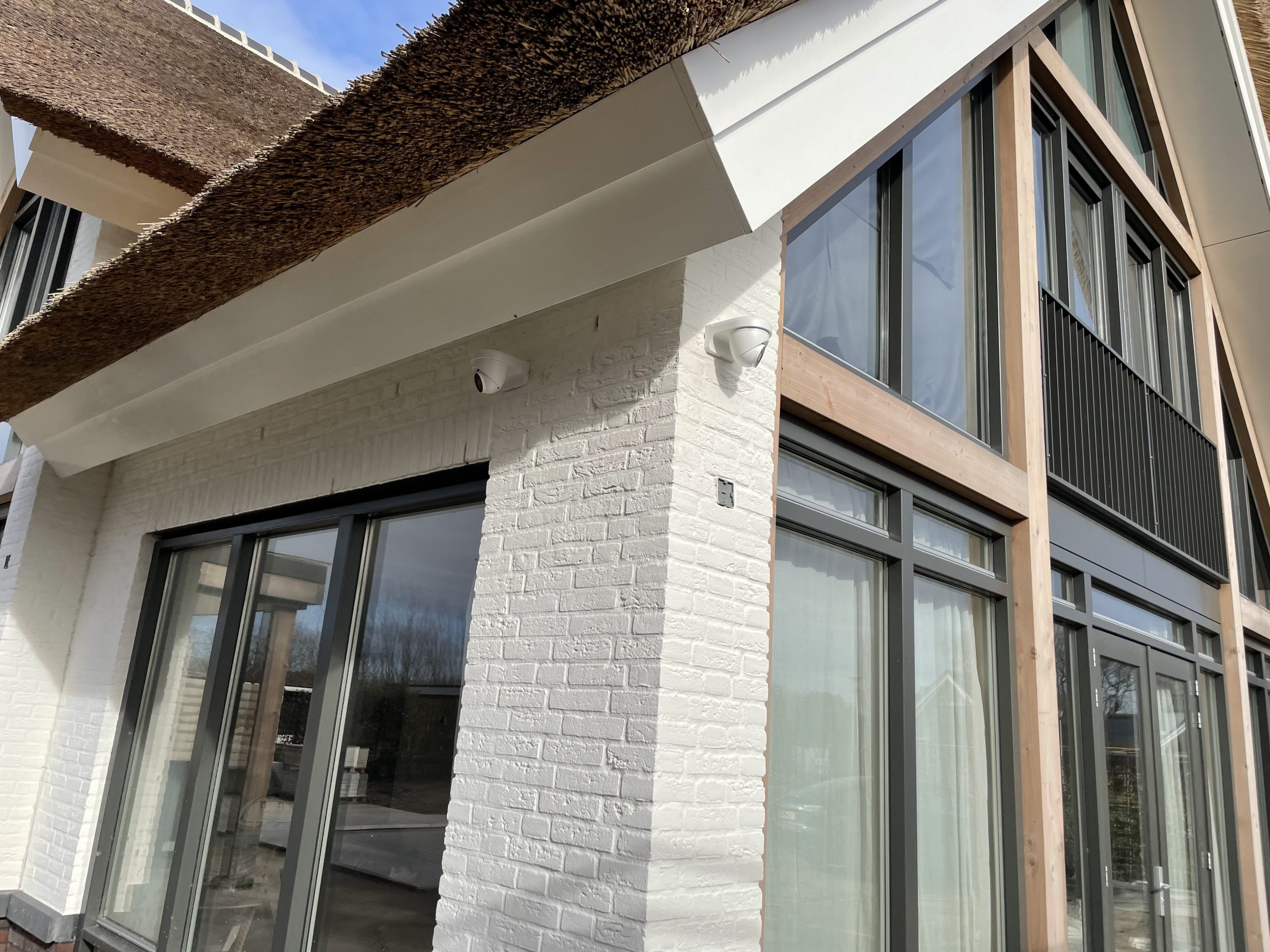 Twee witte camera&rsquo;s onder het boeideel van een rietgedekte villa