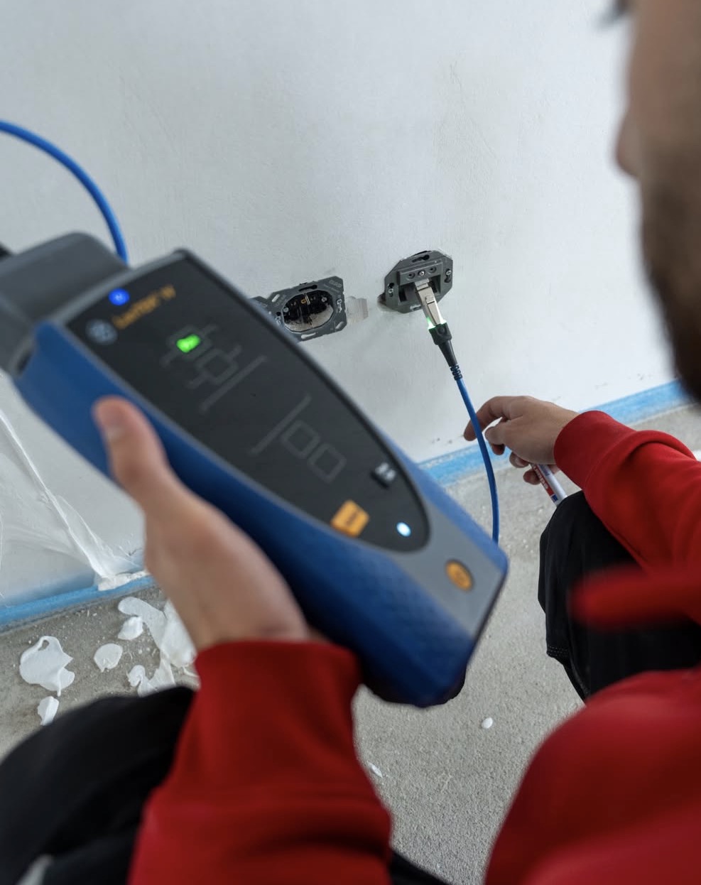 Kabeltester aangesloten op een netwerkaansluiting in de wand