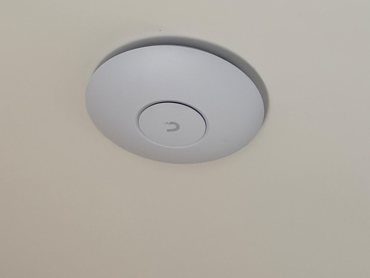 Wit rond access point strak tegen een wit plafond
