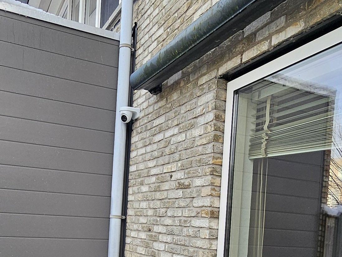 Witte camera aan de achtergevel van een woning, naast de tuindeur