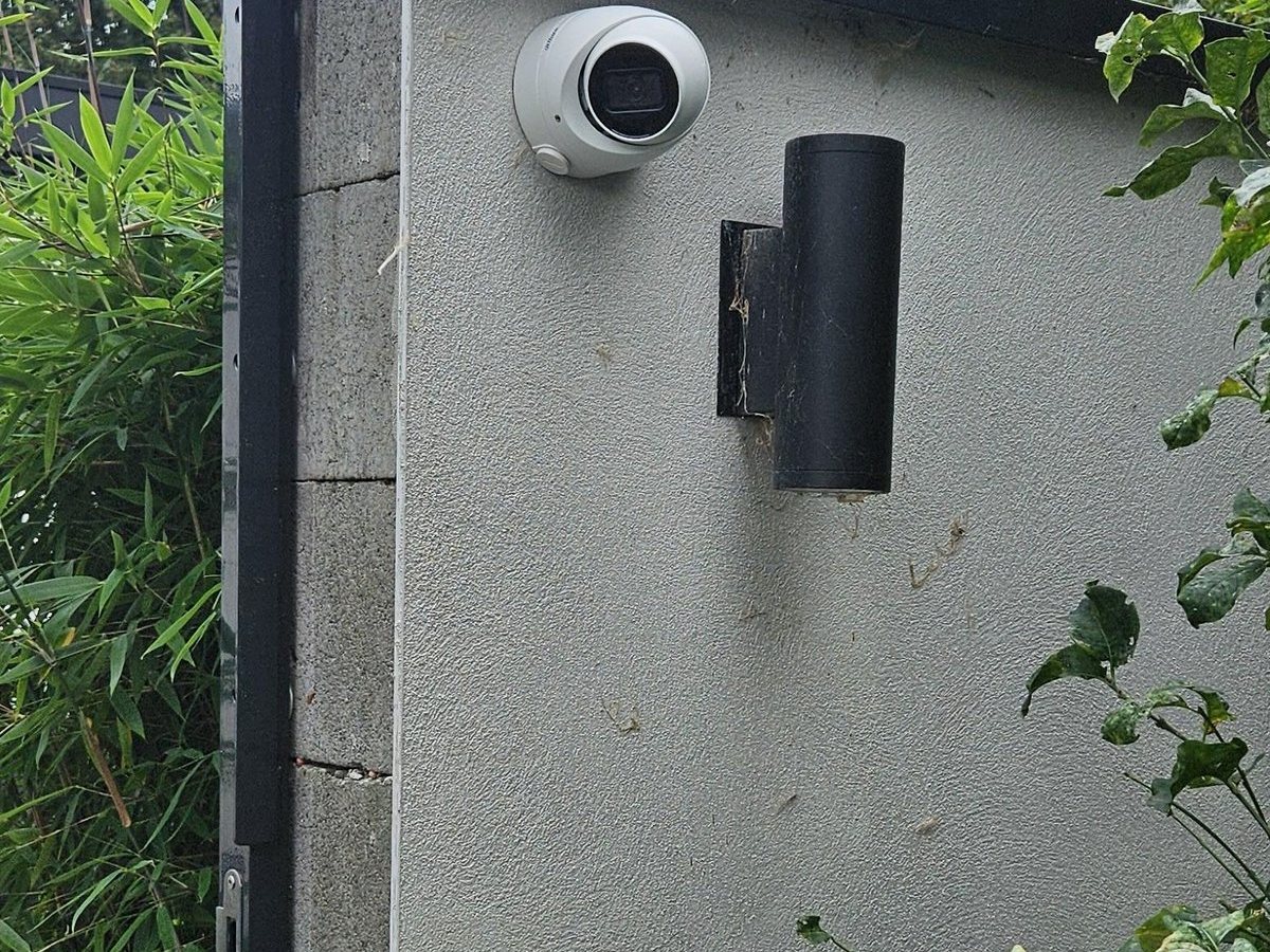 Witte camera op de muur naast de achterpoort, gericht op de steeg achter de tuin