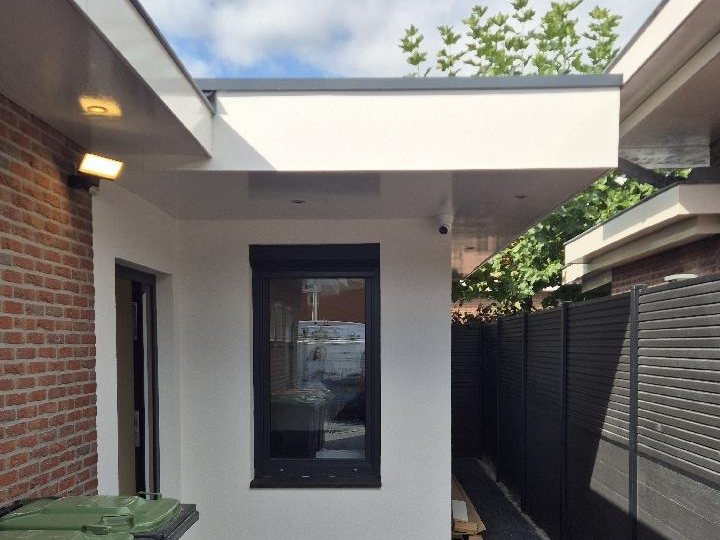 Camera onder de overstek boven een smal zijpad langs een woning