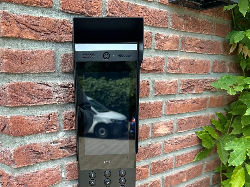 Zwart intercompaneel met camera, scherm en toetsenbord op een bakstenen gevel
