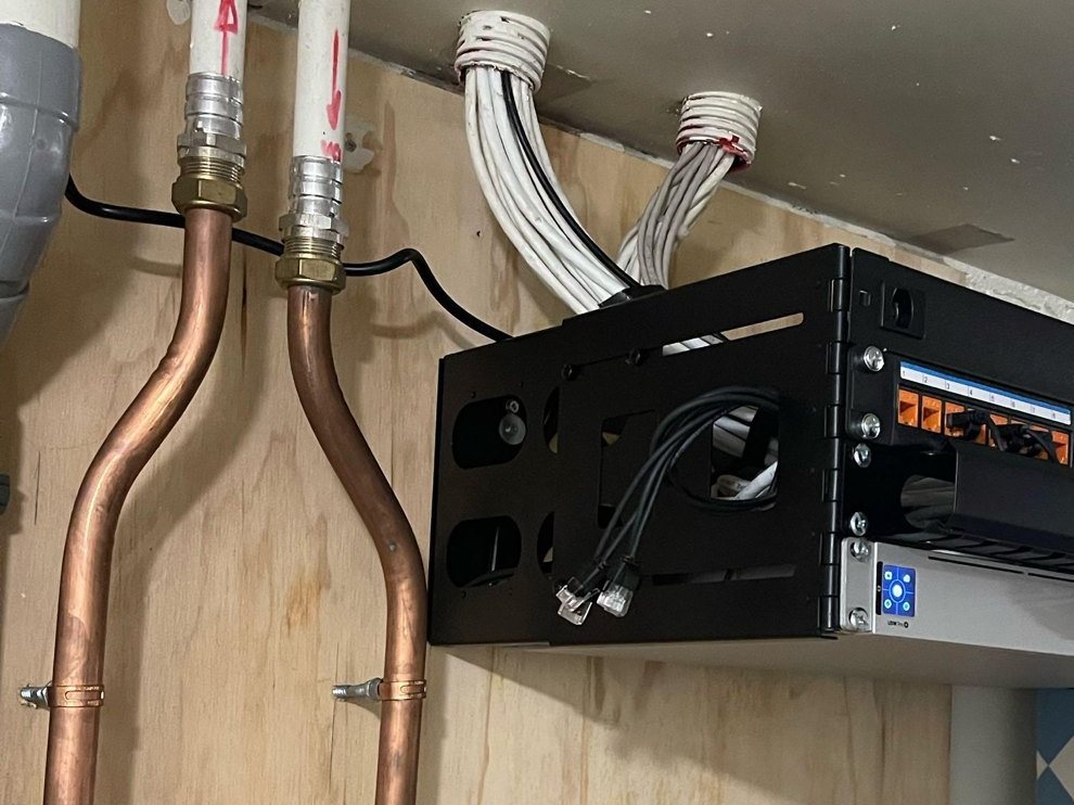 Klein zwart patchrek met UniFi-switch aan een houten wand in een woning