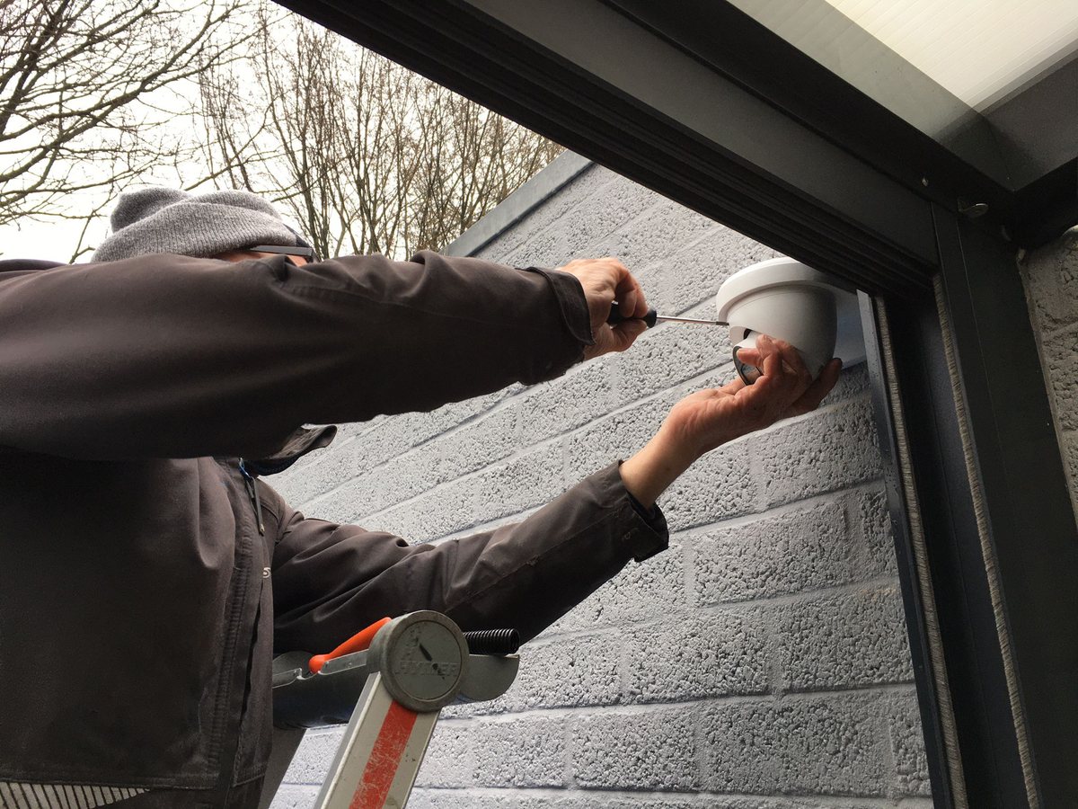 Monteur op een trap hangt een witte domecamera op aan een vakantiewoning