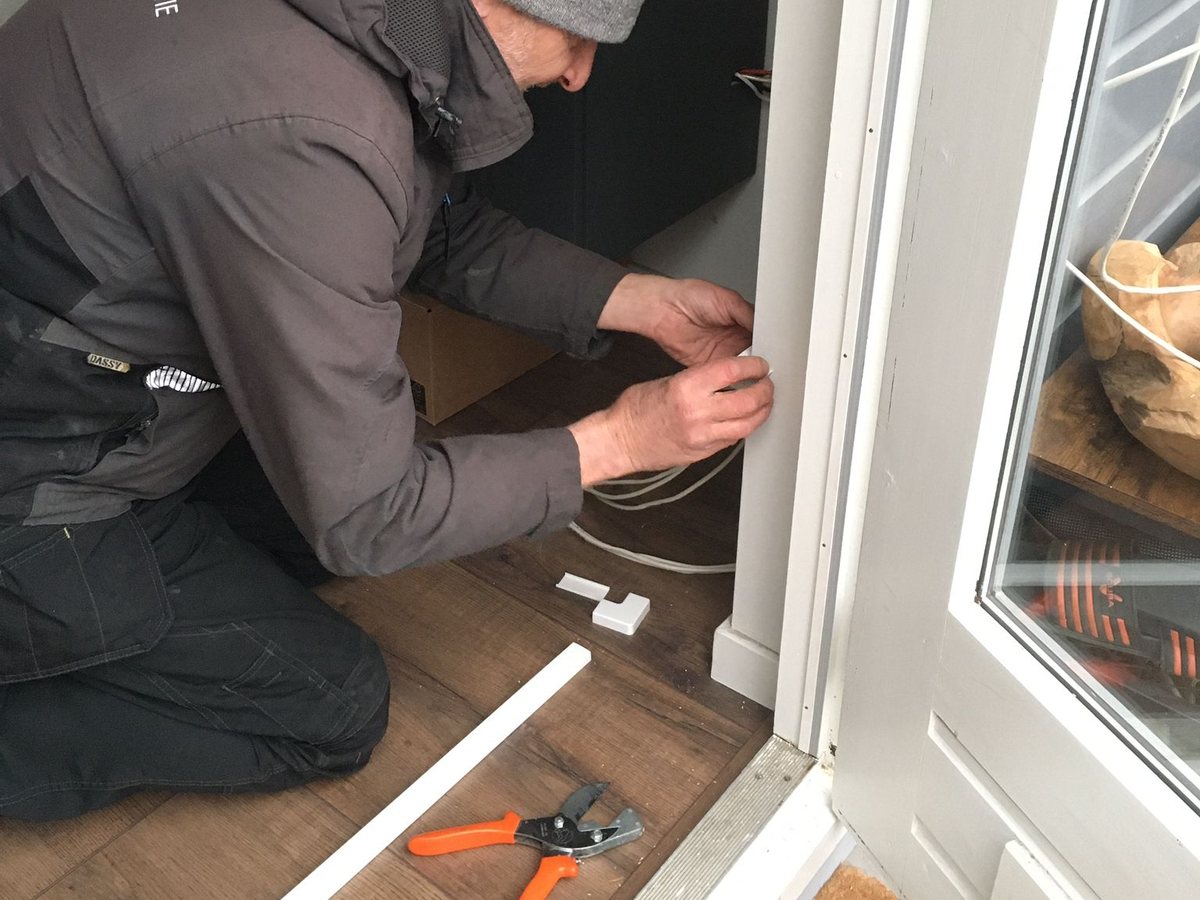 Monteur legt een kabel weggewerkt langs het kozijn van een tuindeur