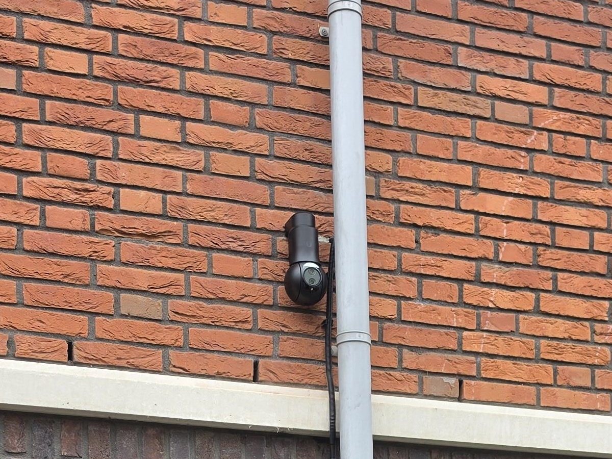 Zwarte bestuurbare UniFi-camera op een muurarm aan een bakstenen gevel