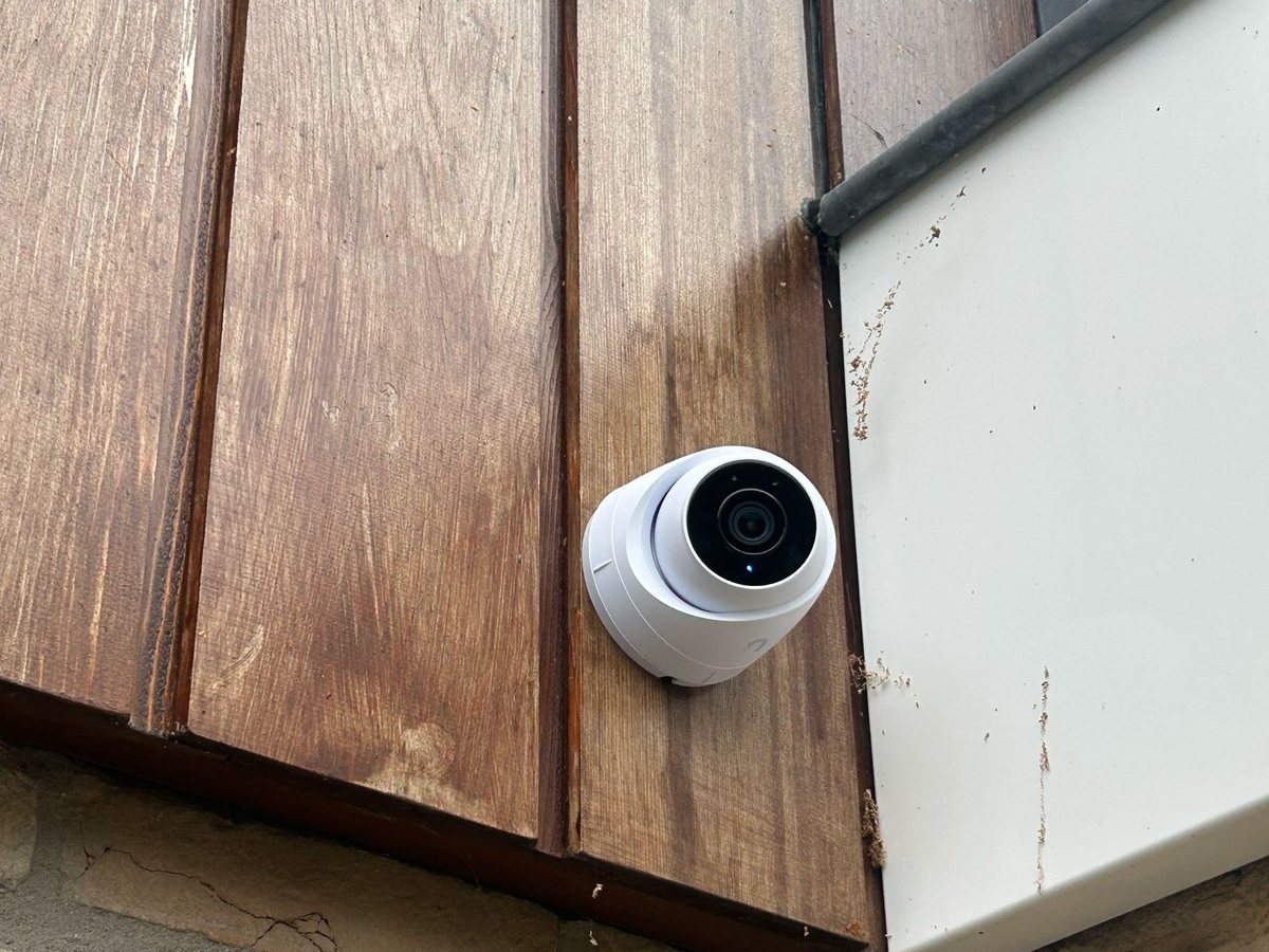 Witte UniFi-turretcamera op de hoek van een gevel met houten bekleding