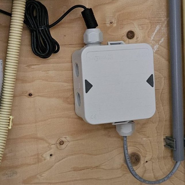 Witte aansluitdoos voor de voeding van de deurbel op een houten plaat, met de kabels weggewerkt