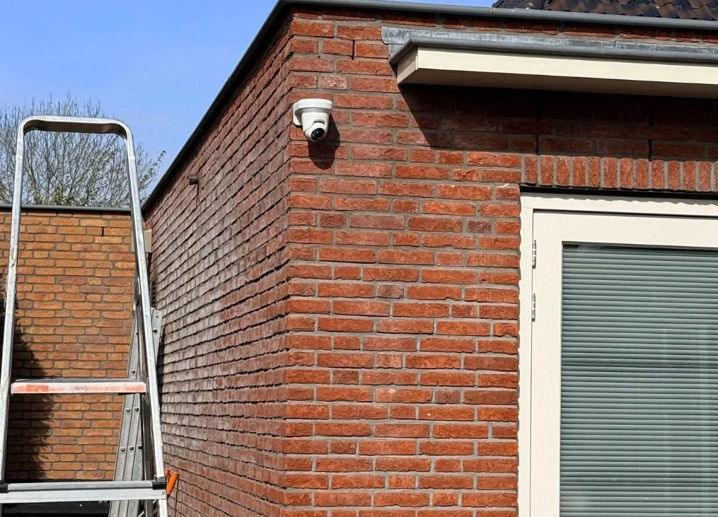 Witte camera hoog op de bakstenen hoek van de woning, met een ladder ernaast