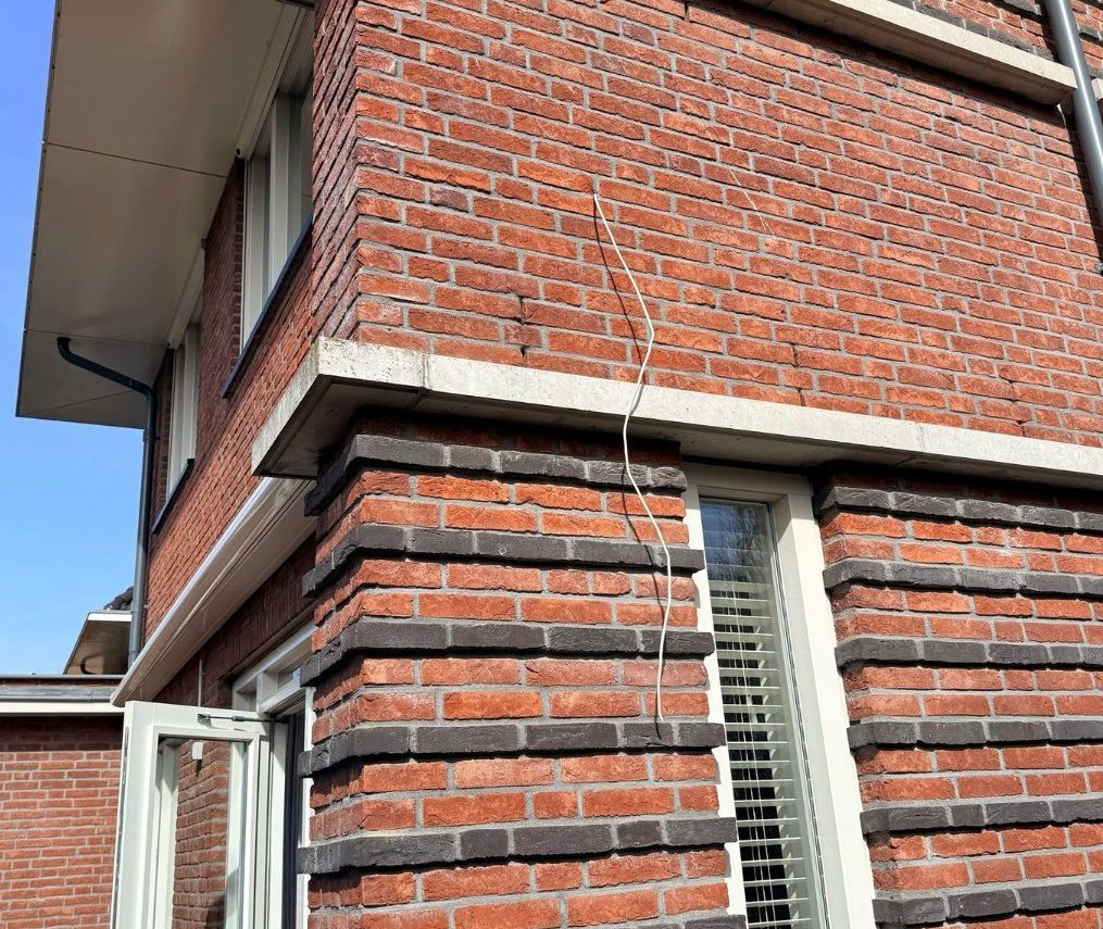 Camerakabel langs de bakstenen hoek van de woning naar het raamkozijn