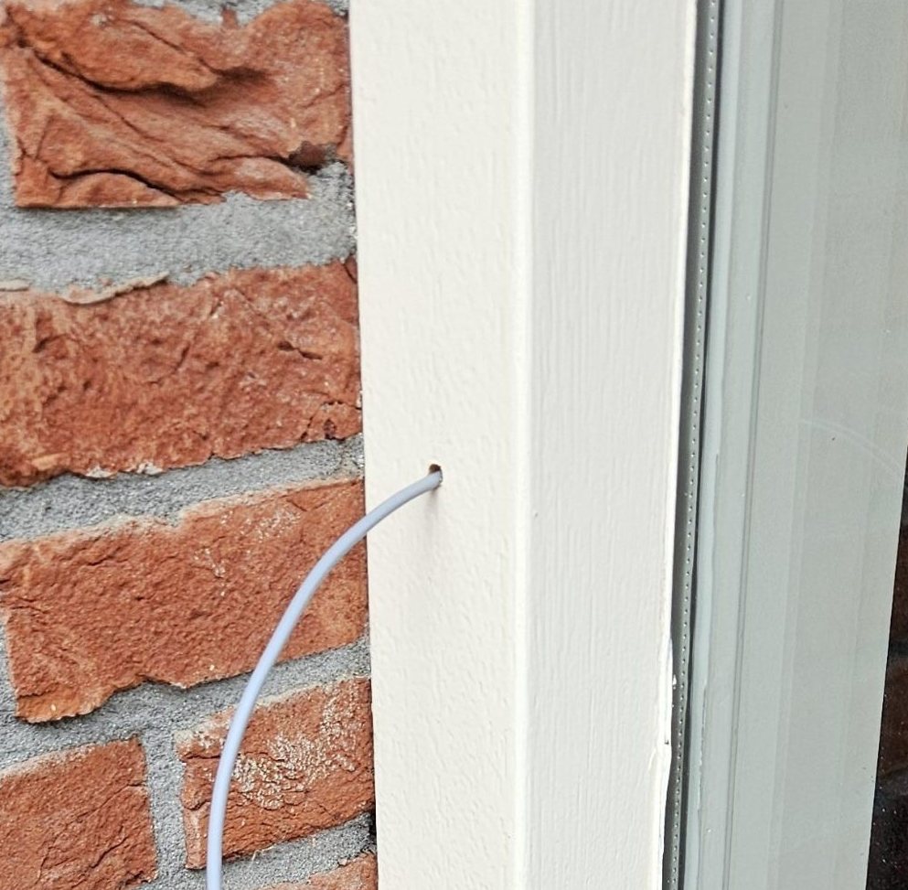 Kabel voor de deurbel door een geboord gaatje in het witte deurkozijn