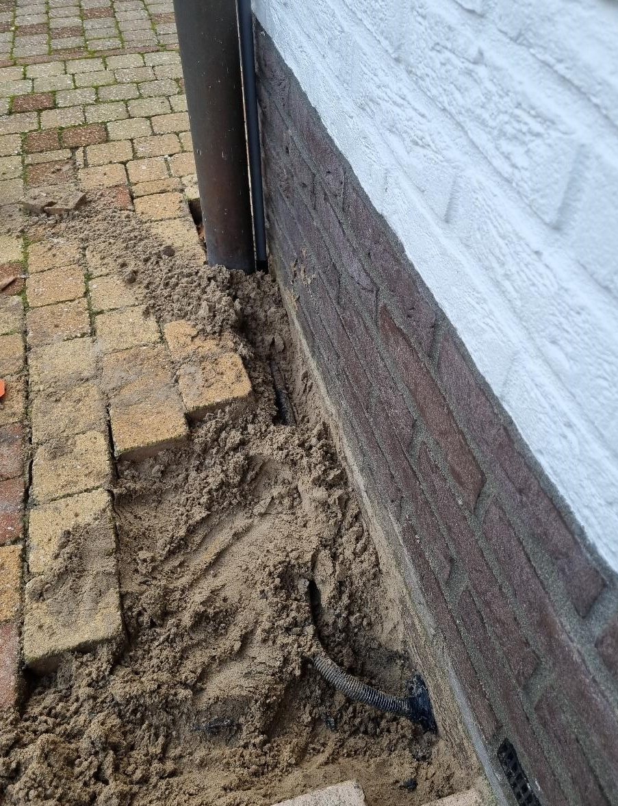 Opengelegde bestrating langs de fundering met een zwarte kabelbuis erin