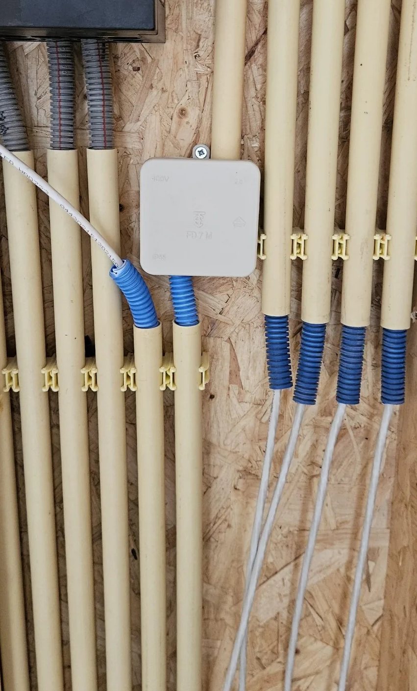 Kelderwand met een rij installatiebuizen op clips en blauwe flexbuisjes met netwerkkabels