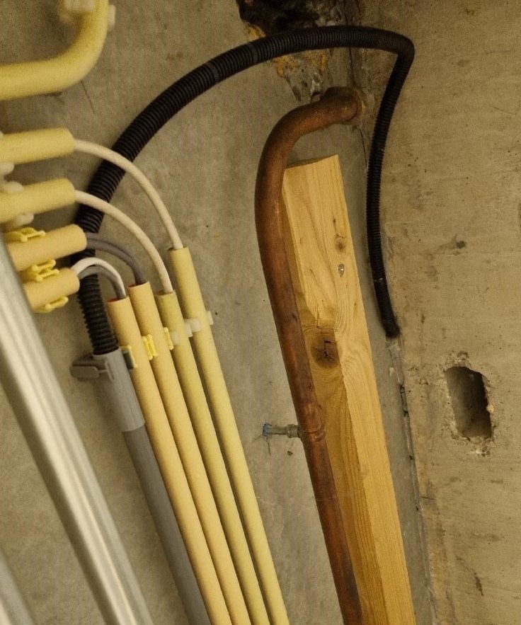 Zwarte flexbuis met netwerkkabel langs leidingen in een kruipruimte