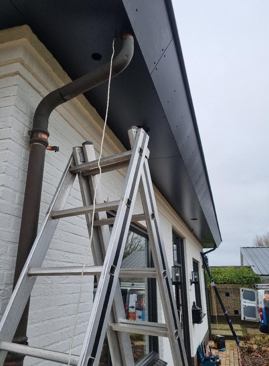 Ladder tegen de witte gevel, met een trekdraad die uit een boring in het zwarte boeideel hangt