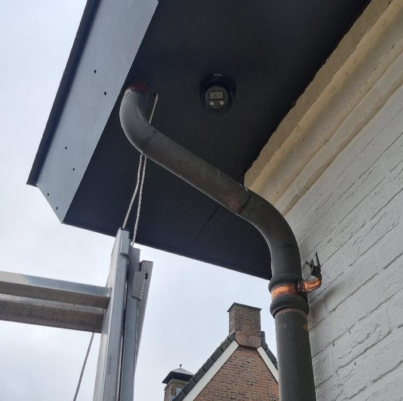 Zwarte camera vlak in het zwarte boeideel van een woning, naast de regenpijp